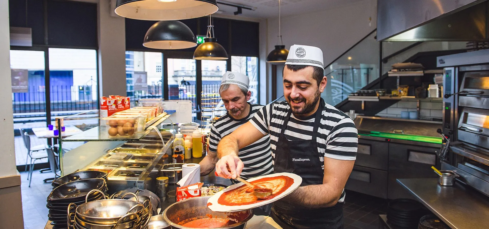 Chefs hand-making pizza in an open PizzaExpress kitchen, the dine-in visit the scheme rewards most